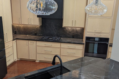 Danish kitchen photo in Houston with an integrated sink, shaker cabinets, light wood cabinets, granite countertops, black backsplash, granite backsplash, black appliances and black countertops