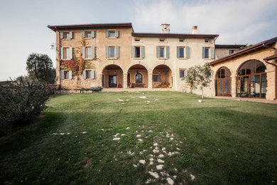 Esempio della facciata di una casa grande country a tre piani in pietra e intonaco con copertura in tegole