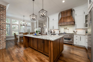Elegant l-shaped medium tone wood floor and brown floor eat-in kitchen photo with a farmhouse sink, shaker cabinets, white cabinets, granite countertops, white backsplash, ceramic backsplash, stainless steel appliances, an island and gray countertops