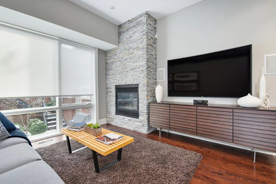 Example of a mid-sized trendy open concept medium tone wood floor and brown floor living room design in Chicago with gray walls, a standard fireplace, a stone fireplace and a wall-mounted tv