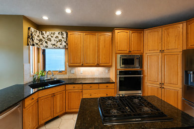Inspiration for a large timeless l-shaped ceramic tile and beige floor enclosed kitchen remodel in Edmonton with an undermount sink, raised-panel cabinets, medium tone wood cabinets, granite countertops, beige backsplash, ceramic backsplash, stainless steel appliances, an island and black countertops