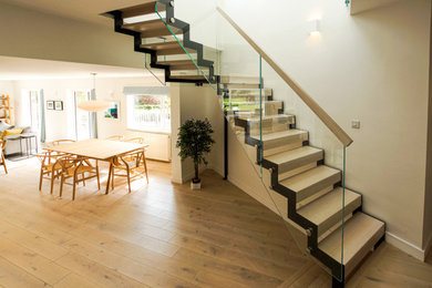 This is an example of a medium sized modern metal l-shaped glass railing staircase in Surrey with wood risers.