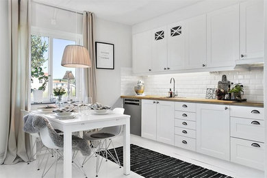 Photo of a mid-sized country single-wall open plan kitchen in Gothenburg with a drop-in sink, shaker cabinets, white cabinets, wood benchtops, white splashback, subway tile splashback, no island and stainless steel appliances.
