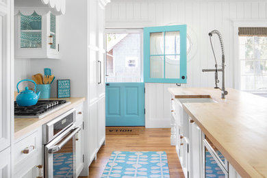 Open concept kitchen - coastal galley medium tone wood floor open concept kitchen idea in Boston with a farmhouse sink, recessed-panel cabinets, white cabinets, wood countertops, white backsplash, wood backsplash, paneled appliances and an island
