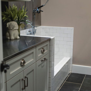 Diseño de lavadero multiusos, de estilo de casa de campo, grande, con fregadero de un seno, armarios estilo shaker, puertas de armario blancas, encimera de acero inoxidable, paredes beige, suelo de baldosas de cerámica, lavadora y secadora juntas y suelo gris