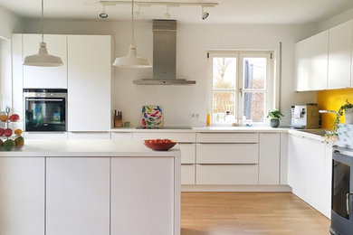 Photo of a large contemporary l-shaped eat-in kitchen in Munich with an integrated sink, flat-panel cabinets, white cabinets, yellow splashback, stainless steel appliances, medium hardwood floors, a peninsula and white benchtop.
