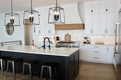 This is an example of a large transitional l-shaped open plan kitchen in Other with a farmhouse sink, flat-panel cabinets, white cabinets, quartz benchtops, white splashback, porcelain splashback, stainless steel appliances, light hardwood floors, with island, brown floor, white benchtop and recessed.