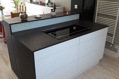 This is an example of a mid-sized contemporary u-shaped eat-in kitchen in Angers with an undermount sink, beaded inset cabinets, white cabinets, solid surface benchtops, black splashback, slate splashback, panelled appliances, laminate floors, with island, white floor and black benchtop.