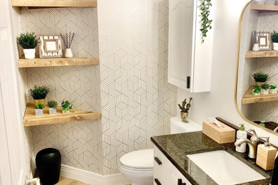 Inspiration for a vinyl floor and wallpaper powder room remodel in Other with white cabinets, a one-piece toilet, white walls, an undermount sink, granite countertops, black countertops and a built-in vanity