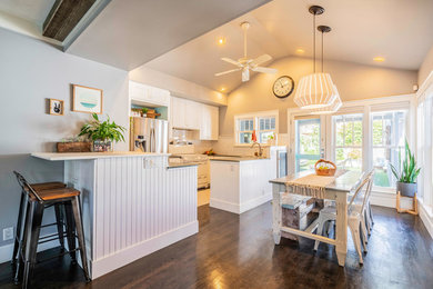 Example of a mid-sized eclectic u-shaped brown floor and dark wood floor eat-in kitchen design in Los Angeles with shaker cabinets, white cabinets, solid surface countertops, white backsplash, ceramic backsplash, white appliances, a peninsula and green countertops