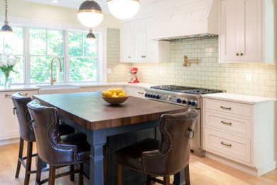 Inspiration for a mid-sized transitional l-shaped kitchen in Boston with a farmhouse sink, beaded inset cabinets, white cabinets, quartz benchtops, green splashback, ceramic splashback, stainless steel appliances, light hardwood floors, with island and white benchtop.