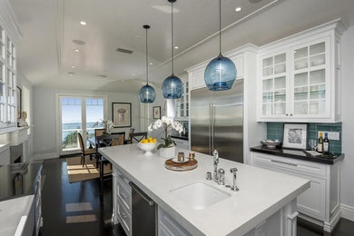Inspiration for a large transitional galley laminate floor and brown floor eat-in kitchen remodel in Los Angeles with a drop-in sink, glass-front cabinets, white cabinets, solid surface countertops, blue backsplash, ceramic backsplash, stainless steel appliances and an island