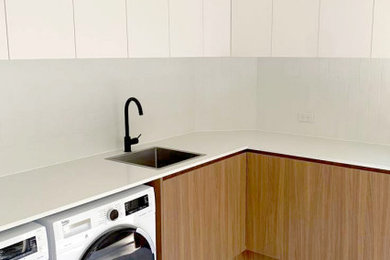 This is an example of a mid-sized l-shaped dedicated laundry room in Townsville with a drop-in sink and a side-by-side washer and dryer.
