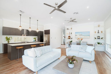 This is an example of a mid-sized open concept living room in Brisbane with white walls, light hardwood floors, a wall-mounted tv and brown floor.