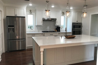 Eat-in kitchen - mid-sized transitional single-wall medium tone wood floor and brown floor eat-in kitchen idea in Other with a farmhouse sink, flat-panel cabinets, white cabinets, quartz countertops, white backsplash, subway tile backsplash, stainless steel appliances and an island