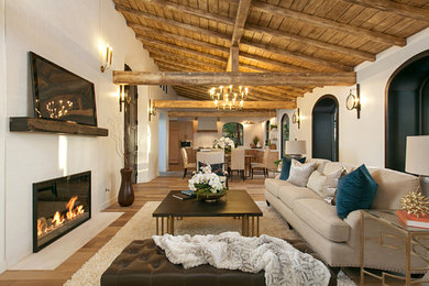 Mediterranean open concept living room in San Diego with white walls, medium hardwood floors, a standard fireplace, a tile fireplace surround, a wall-mounted tv and brown floor.