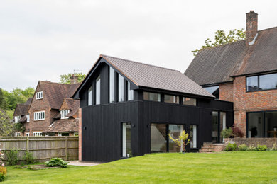 Ejemplo de fachada de casa negra y roja contemporánea de tamaño medio con revestimiento de madera, tejado a dos aguas y tejado de teja de barro