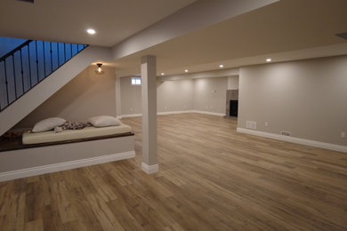 Inspiration for a contemporary laminate floor and brown floor basement remodel in Toronto with gray walls, a standard fireplace and a plaster fireplace