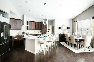 Inspiration for a mid-sized contemporary l-shaped dark wood floor and brown floor open concept kitchen remodel in Milwaukee with a farmhouse sink, flat-panel cabinets, dark wood cabinets, solid surface countertops, metallic backsplash, metal backsplash, stainless steel appliances and an island