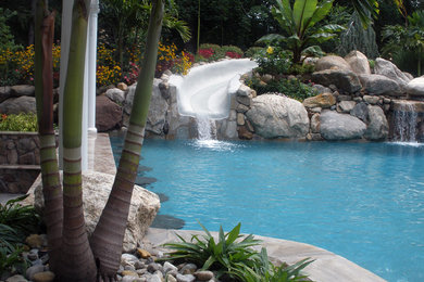 Photo of an expansive tropical backyard custom-shaped natural pool in New York with natural stone pavers and a hot tub.