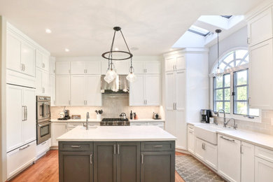 Inspiration for a large transitional u-shaped medium tone wood floor and brown floor open concept kitchen remodel in San Francisco with a farmhouse sink, shaker cabinets, white cabinets, quartz countertops, gray backsplash, subway tile backsplash, paneled appliances, an island and white countertops