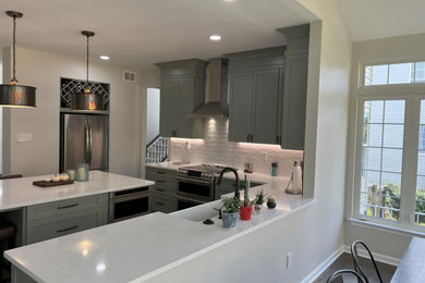 Eat-in kitchen - mid-sized transitional l-shaped medium tone wood floor and gray floor eat-in kitchen idea in DC Metro with a farmhouse sink, shaker cabinets, green cabinets, quartz countertops, white backsplash, porcelain backsplash, stainless steel appliances, an island and white countertops