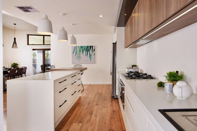 Design ideas for a large scandinavian galley kitchen pantry in Other with a drop-in sink, flat-panel cabinets, white cabinets, quartz benchtops, white splashback, ceramic splashback, stainless steel appliances, medium hardwood floors, with island, brown floor and white benchtop.
