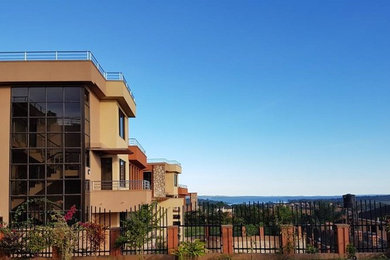 Large trendy brown three-story adobe exterior home photo in Other