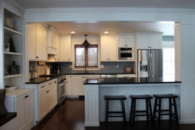 Example of a mid-sized transitional l-shaped dark wood floor and brown floor eat-in kitchen design in Other with an undermount sink, shaker cabinets, white cabinets, solid surface countertops, stainless steel appliances and a peninsula
