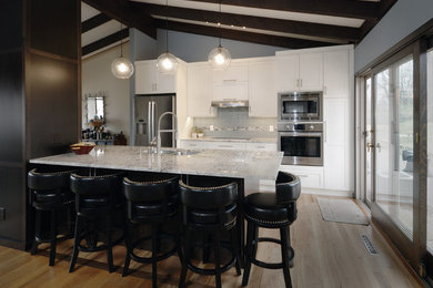 Inspiration for a mid-sized transitional galley light wood floor and yellow floor open concept kitchen remodel in Minneapolis with an undermount sink, recessed-panel cabinets, white cabinets, granite countertops, blue backsplash, glass tile backsplash, stainless steel appliances, a peninsula and white countertops