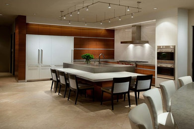 Large trendy l-shaped travertine floor eat-in kitchen photo with flat-panel cabinets, dark wood cabinets, white appliances, an undermount sink, concrete countertops, white backsplash, stone slab backsplash and an island