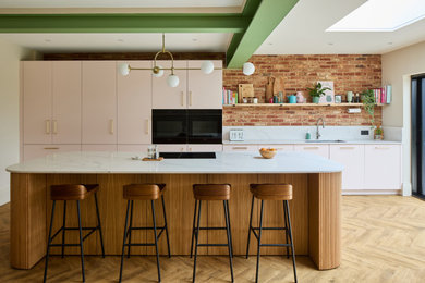 This is an example of a medium sized contemporary single-wall open plan kitchen in London with flat-panel cabinets, pink cabinets, engineered stone countertops, an island and white worktops.
