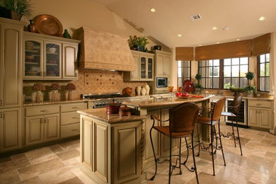 This is an example of a large mediterranean kitchen in San Francisco with beige cabinets, granite benchtops, beige splashback, glass tile splashback, stainless steel appliances, travertine floors and with island.