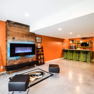 This is an example of a medium sized modern walk-out basement in Kansas City with orange walls, concrete flooring and a ribbon fireplace.