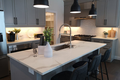 Inspiration for a farmhouse l-shaped medium tone wood floor and brown floor kitchen remodel in Other with an undermount sink, shaker cabinets, gray cabinets, quartz countertops, white backsplash, subway tile backsplash, stainless steel appliances, an island and white countertops