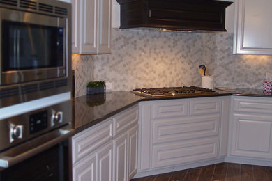 Eat-in kitchen - large transitional l-shaped dark wood floor and brown floor eat-in kitchen idea in Austin with a farmhouse sink, raised-panel cabinets, white cabinets, granite countertops, gray backsplash, stainless steel appliances and an island