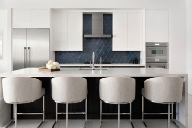 Large trendy l-shaped porcelain tile, white floor and coffered ceiling open concept kitchen photo in Miami with a single-bowl sink, flat-panel cabinets, white cabinets, quartz countertops, blue backsplash, glass tile backsplash, stainless steel appliances, an island and white countertops