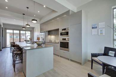 Inspiration for a mid-sized contemporary single-wall medium tone wood floor and gray floor open concept kitchen remodel in Calgary with a single-bowl sink, flat-panel cabinets, gray cabinets, quartz countertops, white backsplash, mosaic tile backsplash, stainless steel appliances and an island