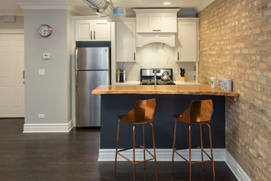 Mid-sized urban galley dark wood floor and brown floor open concept kitchen photo in Chicago with an undermount sink, flat-panel cabinets, white cabinets, wood countertops, white backsplash, marble backsplash, stainless steel appliances and an island