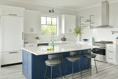 Inspiration for a coastal l-shaped gray floor eat-in kitchen remodel in Atlanta with a farmhouse sink, shaker cabinets, white cabinets, quartz countertops, white backsplash, ceramic backsplash, stainless steel appliances, an island and white countertops