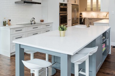 Photo of an expansive transitional u-shaped open plan kitchen in Toronto with an undermount sink, shaker cabinets, white cabinets, quartz benchtops, white splashback, subway tile splashback, stainless steel appliances, medium hardwood floors, with island, brown floor and white benchtop.