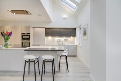Photo of a mid-sized contemporary single-wall open plan kitchen in Glasgow with flat-panel cabinets, panelled appliances, with island and grey floor.