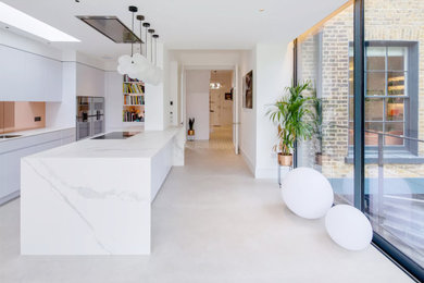 Design ideas for a large contemporary cream and black galley kitchen/diner in London with a double-bowl sink, flat-panel cabinets, white cabinets, marble worktops, metallic splashback, mirror splashback, stainless steel appliances, porcelain flooring, an island, beige floors, white worktops and feature lighting.