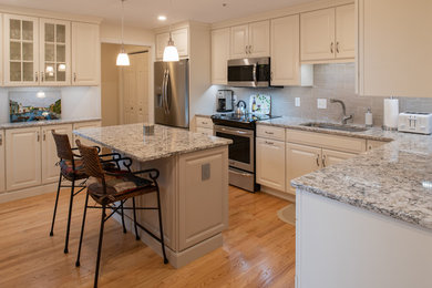 Inspiration for a mid-sized timeless l-shaped light wood floor and brown floor enclosed kitchen remodel in Boston with an undermount sink, raised-panel cabinets, white cabinets, quartz countertops, beige backsplash, subway tile backsplash, stainless steel appliances, an island and gray countertops
