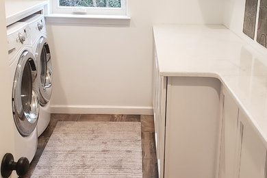 Photo of a mid-sized country galley dedicated laundry room in Detroit with a farmhouse sink, recessed-panel cabinets, white cabinets, marble benchtops, white walls, porcelain floors, an integrated washer and dryer, brown floor and white benchtop.