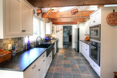 Inspiration for a mid-sized timeless galley slate floor kitchen pantry remodel in Philadelphia with a farmhouse sink, shaker cabinets, white cabinets, soapstone countertops, multicolored backsplash, stainless steel appliances and no island