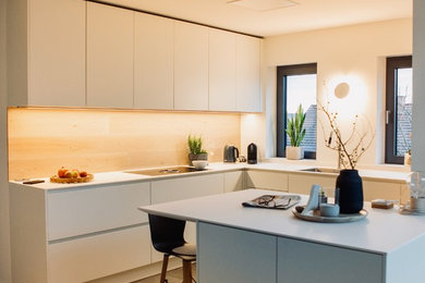 Geschlossene Nordische Küche in L-Form mit Einbauwaschbecken, flächenbündigen Schrankfronten, weißen Schränken, Mineralwerkstoff-Arbeitsplatte, Küchenrückwand in Braun, Rückwand aus Holz, Zementfliesen für Boden, Kücheninsel, beigem Boden und weißer Arbeitsplatte in Frankfurt am Main
