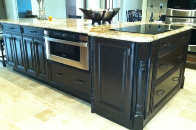 Example of a large classic travertine floor kitchen design in Other with an undermount sink, recessed-panel cabinets, dark wood cabinets, granite countertops, beige backsplash, stone tile backsplash, stainless steel appliances and an island