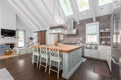 Open concept kitchen - traditional l-shaped dark wood floor, brown floor, exposed beam, shiplap ceiling and vaulted ceiling open concept kitchen idea in Charleston with a farmhouse sink, shaker cabinets, white cabinets, gray backsplash, stainless steel appliances, an island and beige countertops