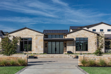 Example of a huge trendy beige two-story stone house exterior design in Dallas with a metal roof and a black roof